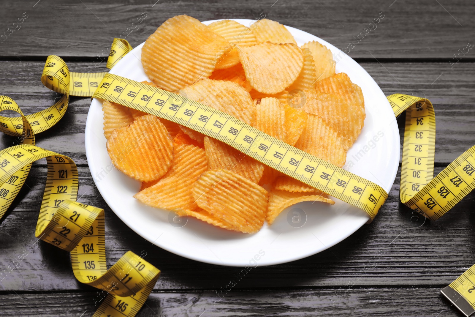 Photo of Plate with potato chips and measuring tape on wooden table. Weight loss concept