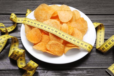 Plate with potato chips and measuring tape on wooden table. Weight loss concept