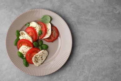 Photo of Delicious Caprese salad with tomatoes, mozzarella, basil and spices on light grey table, top view. Space for text