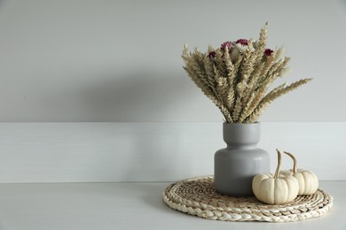 Photo of Beautiful bouquet of dry flowers and small pumpkins on white table near light wall, space for text