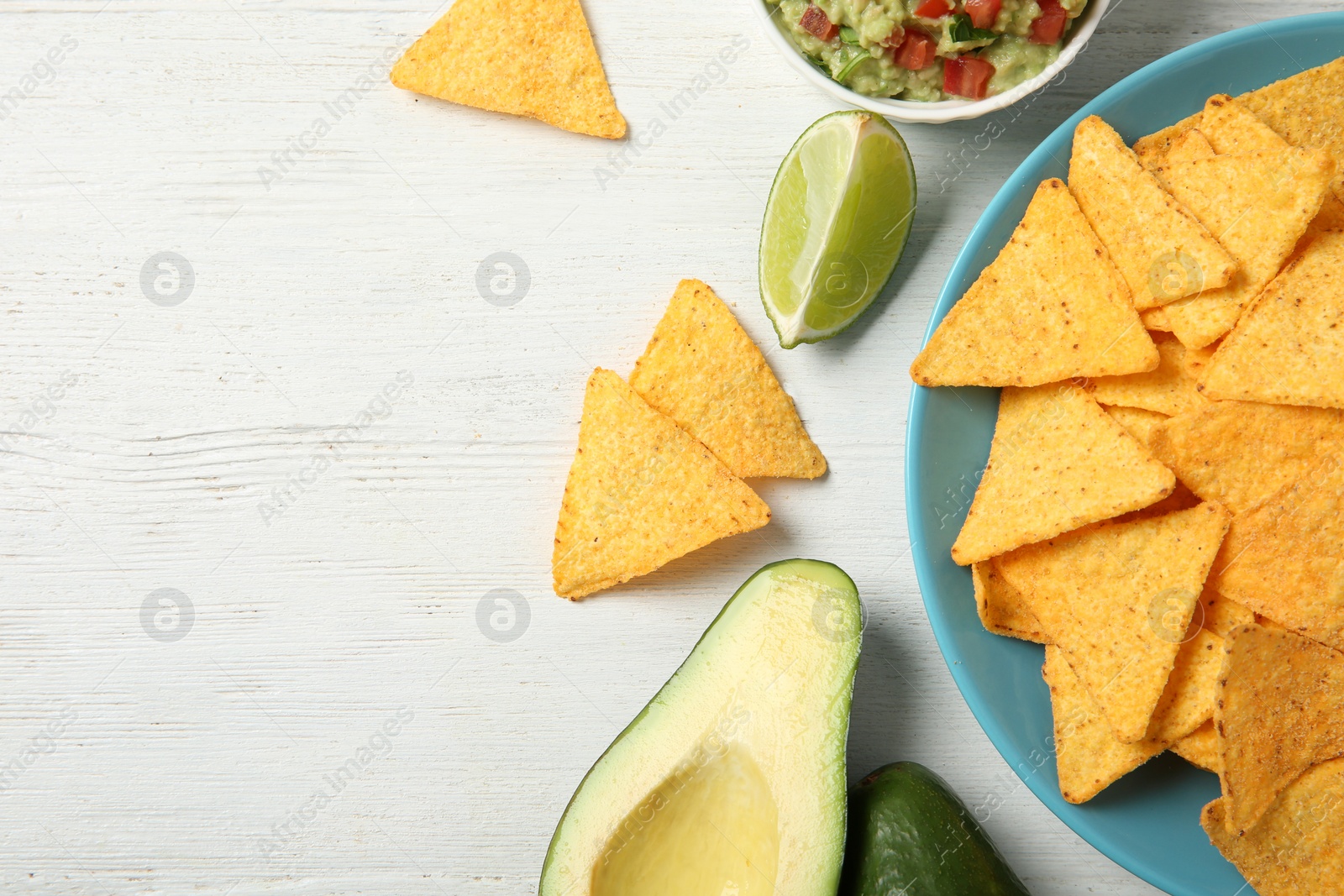 Photo of Plate with delicious mexican nachos chips, guacamole sauce, lime and avocado on white wooden table, flat lay. Space for text