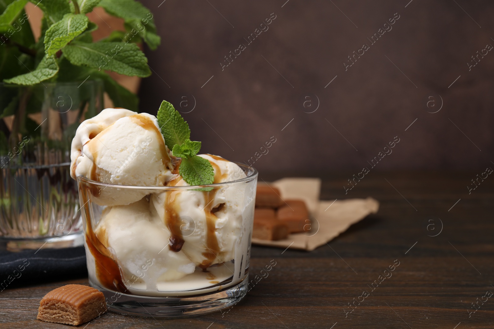 Photo of Scoops of ice cream with caramel sauce, mint leaves and candies on wooden table, closeup. Space for text