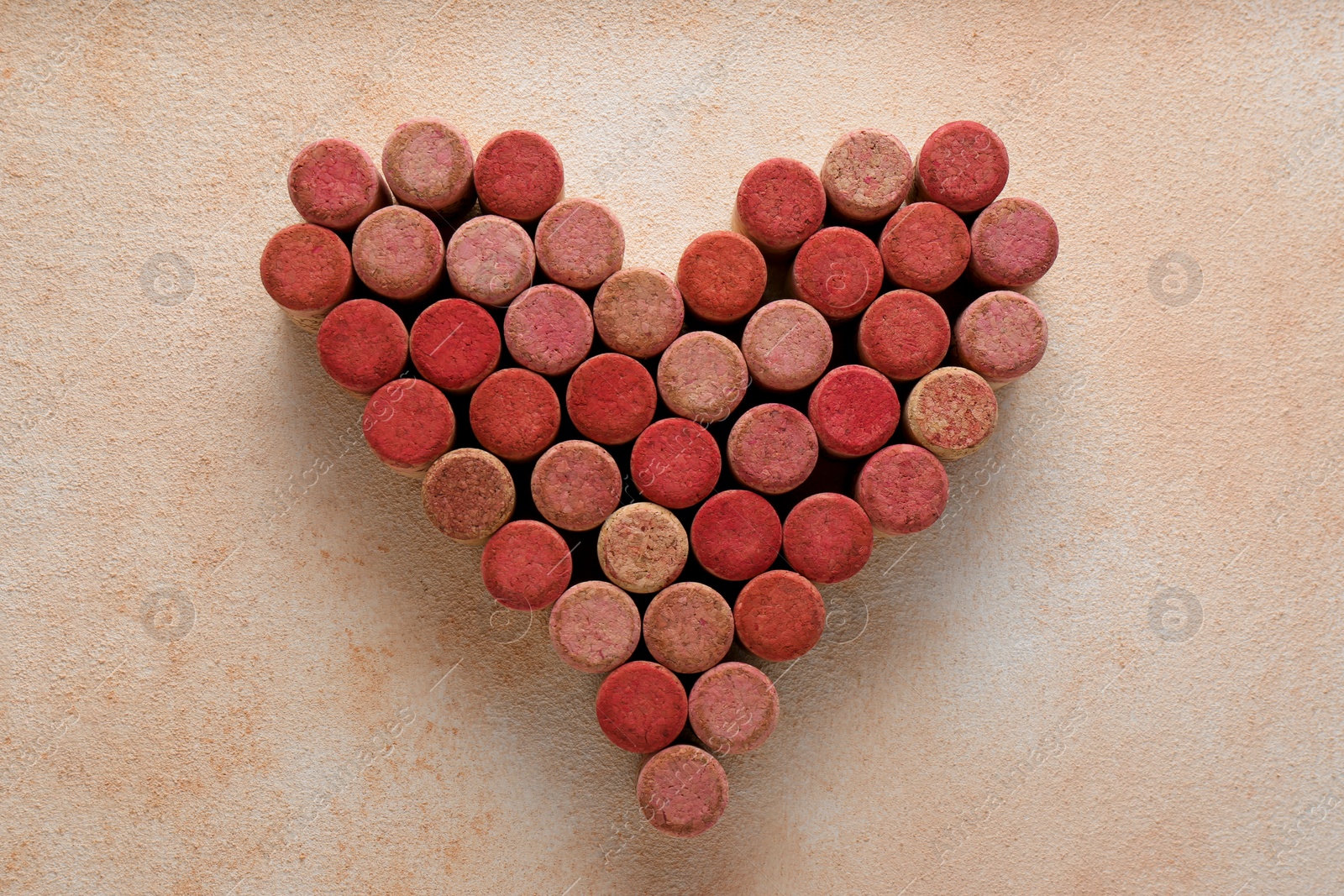 Photo of Heart made of wine bottle corks on textured table, top view