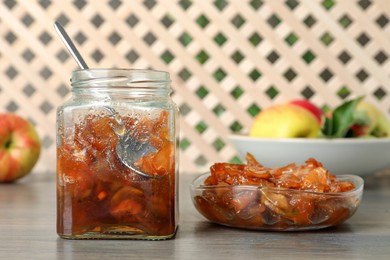 Photo of Tasty apple jam in glass jar and bowl on wooden table
