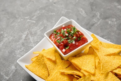 Plate with delicious mexican nachos chips and salsa sauce on grey table, closeup