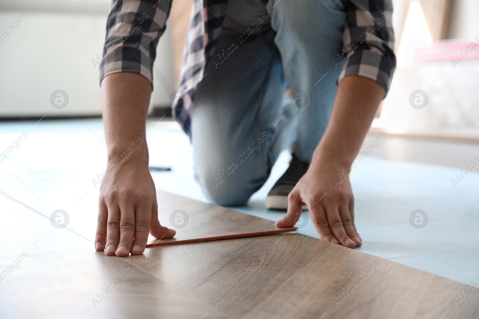 Photo of Worker installing laminated wooden floor indoors, closeup