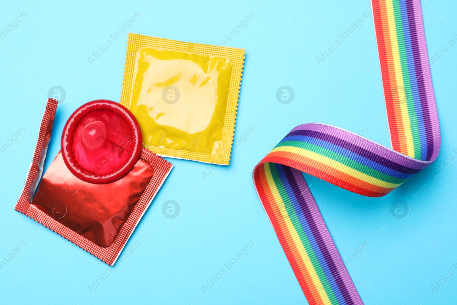 Photo of Colorful condoms and rainbow ribbon on light blue background, flat lay. LGBT concept