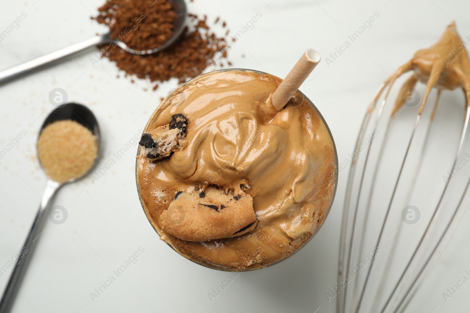 Photo of Glass of delicious dalgona coffee with cookie pieces on white table, flat lay