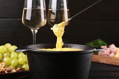 Photo of Dipping grape into fondue pot with melted cheese on table, closeup