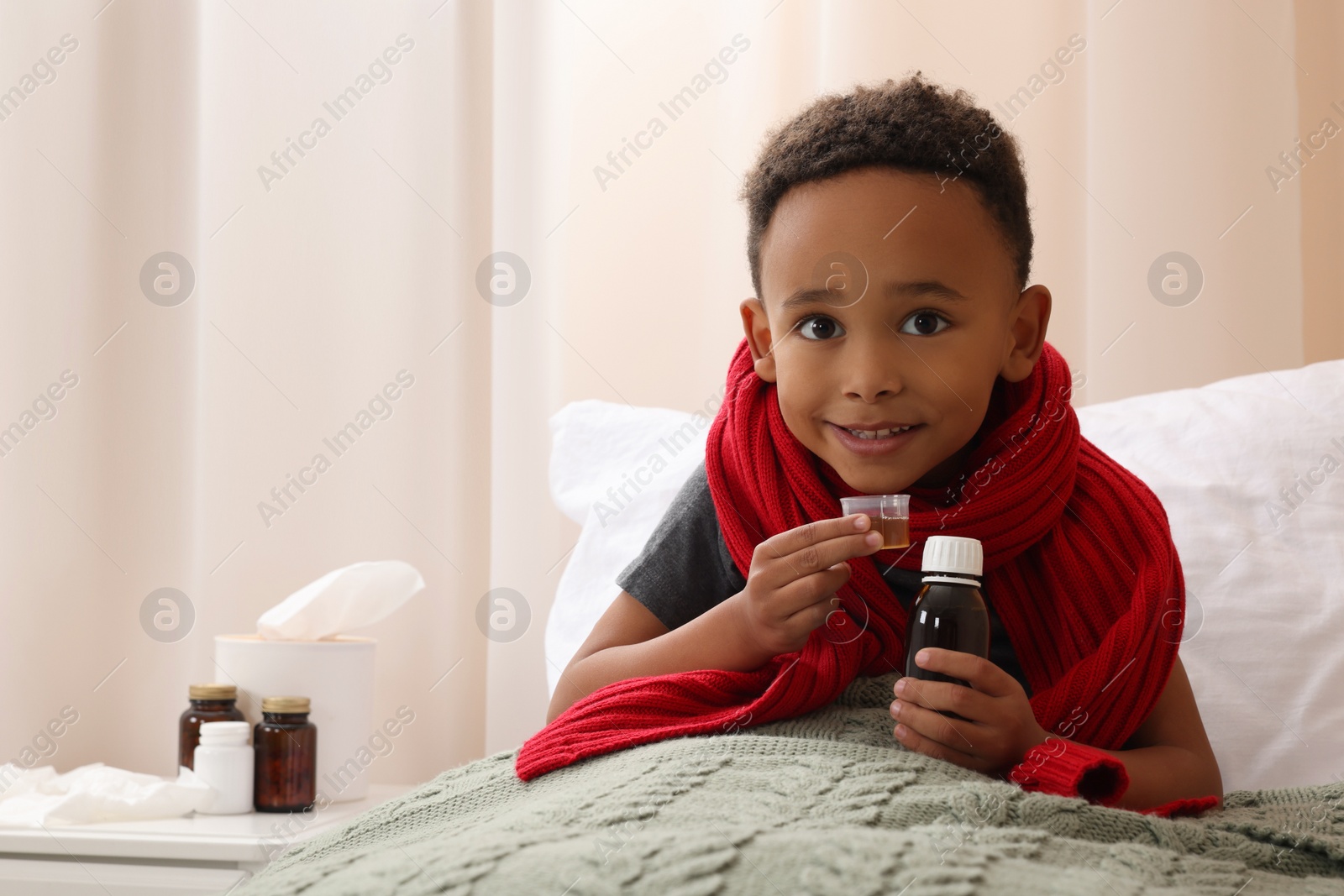 Photo of African-American boy taking cough syrup on bed at home, space for text. Cold medicine