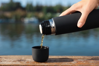 Photo of Woman pouring hot drink from thermos into cap outdoors, closeup