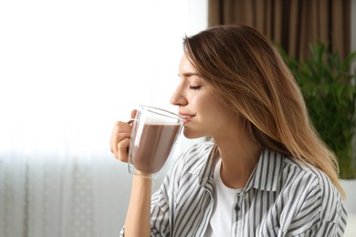 Photo of Young woman drinking chocolate milk in room