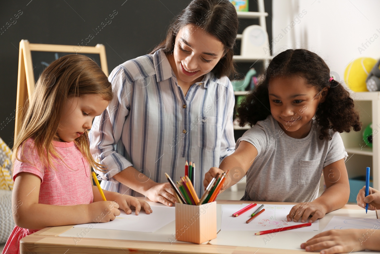 Photo of Cute little children with nursery teacher drawing at table in kindergarten. Indoor activity