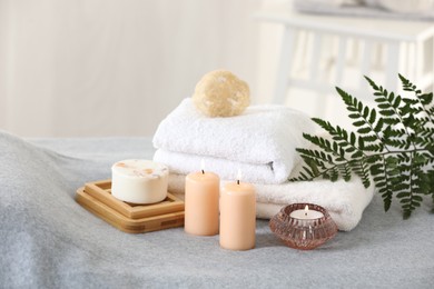 Photo of Spa composition. Burning candles, soap, towels and loofah on soft grey surface