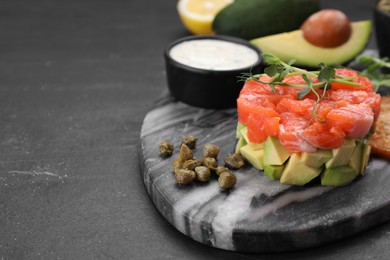 Photo of Delicious salmon tartare served with avocado and sauce on dark table, closeup. Space for text