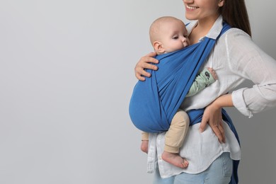 Mother holding her child in sling (baby carrier) on light grey background, closeup. Space for text