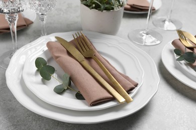 Stylish setting with cutlery and eucalyptus leaves on light grey table, closeup