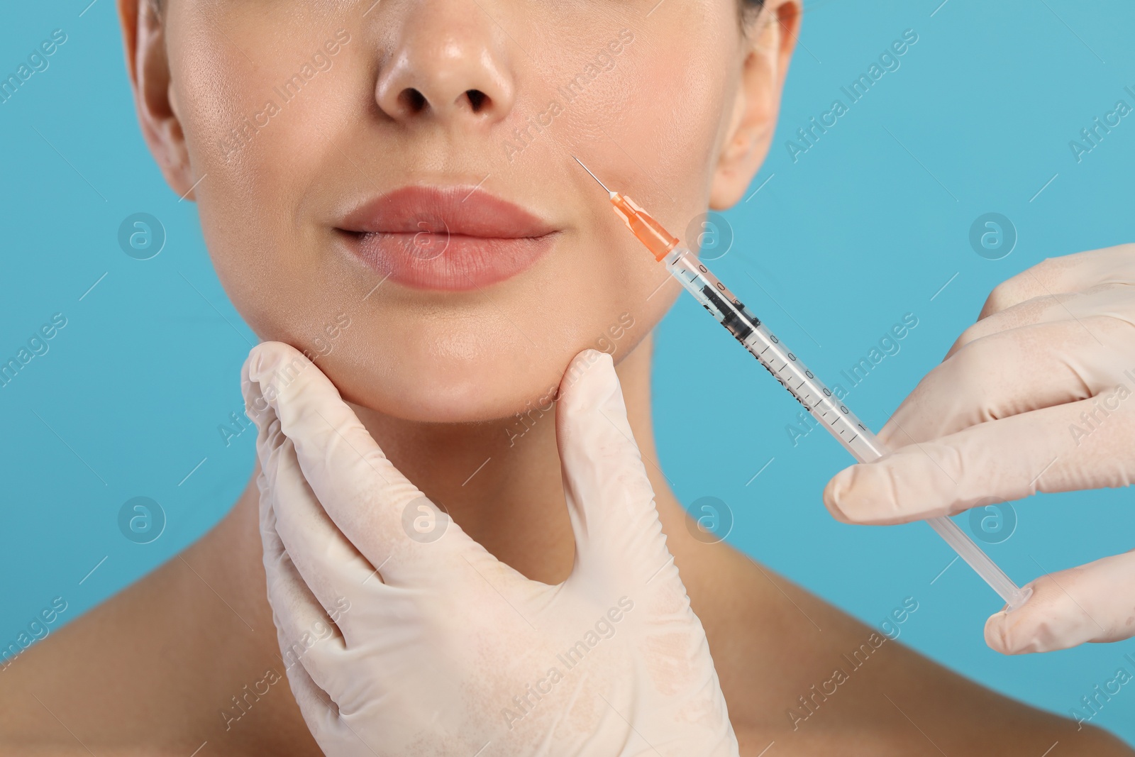 Photo of Doctor giving facial injection to young woman on light blue background, closeup. Cosmetic surgery