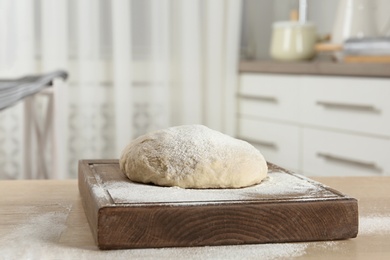 Wooden board with flour and bread dough on table indoors. Space for text