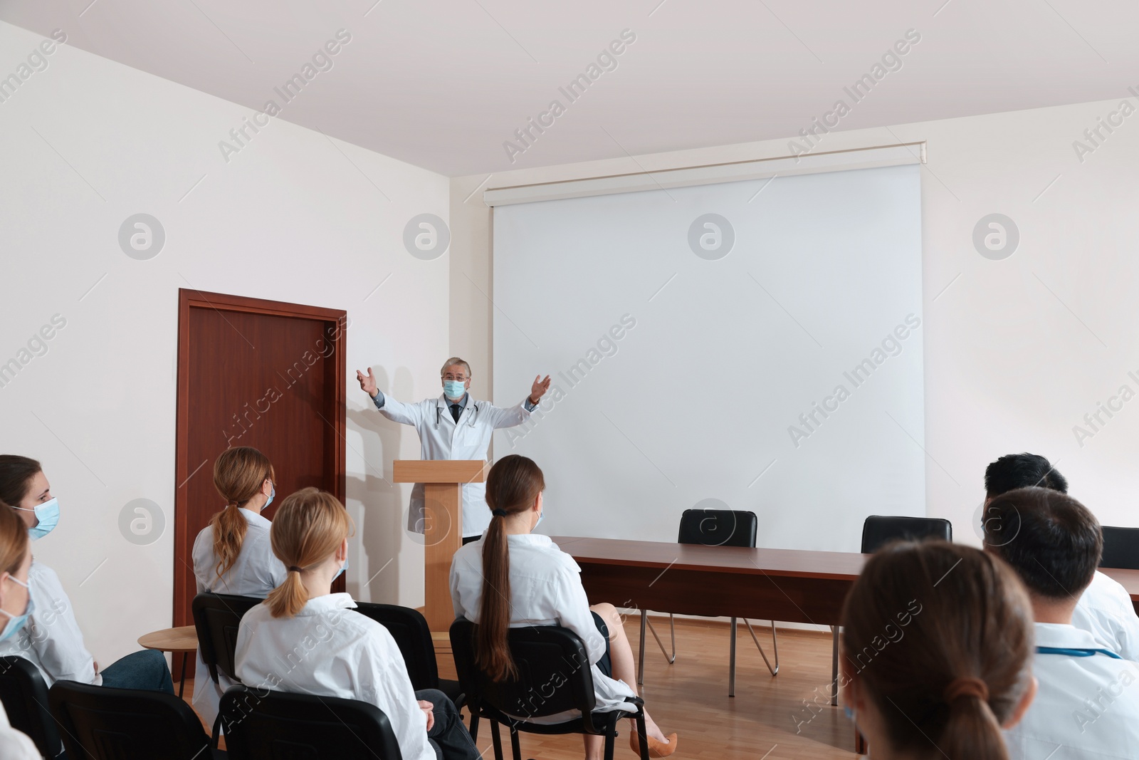 Photo of Senior doctor giving lecture near projection screen in conference room