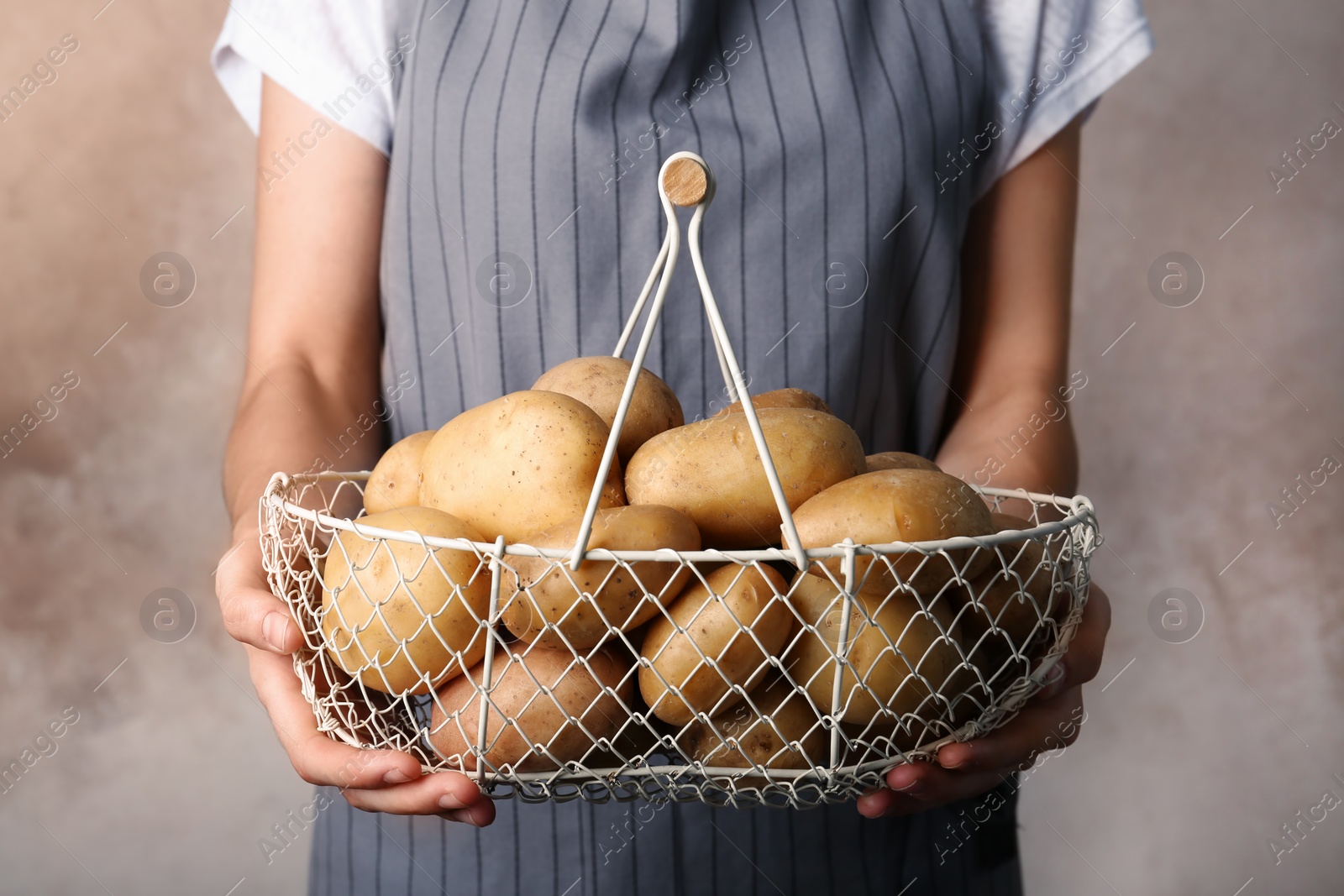 Photo of Person holding basket with fresh organic potatoes on color background