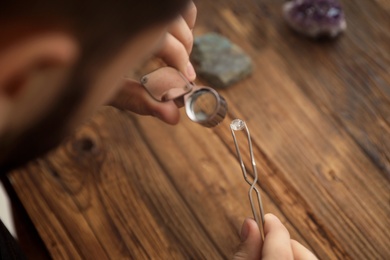 Male jeweler evaluating precious gemstone at table in workshop, closeup