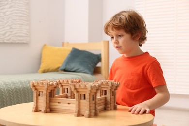 Cute little boy playing with wooden fortress at table in room. Child's toy