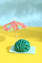 Brain made of plasticine on mini blanket under umbrella against color background