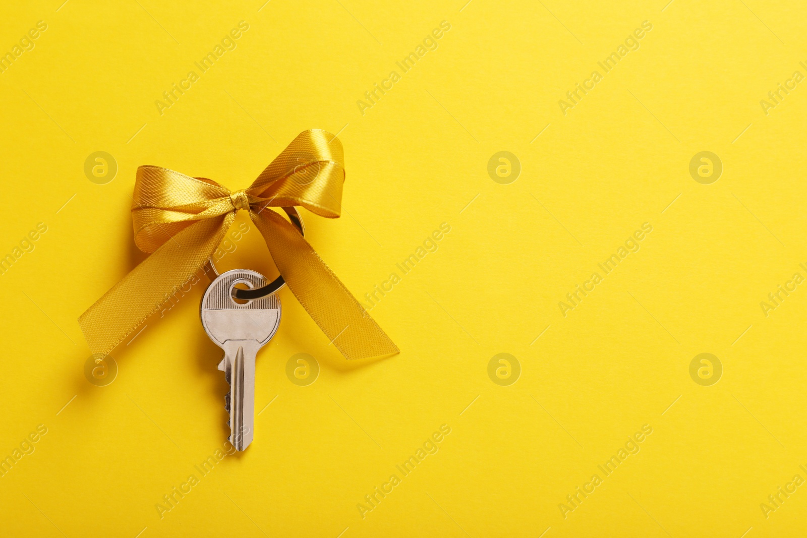 Photo of Key with color bow on yellow background, top view. Space for text. Housewarming party