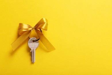 Photo of Key with color bow on yellow background, top view. Space for text. Housewarming party