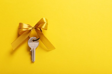 Key with color bow on yellow background, top view. Space for text. Housewarming party