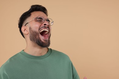 Photo of Handsome young man laughing on beige background, space for text