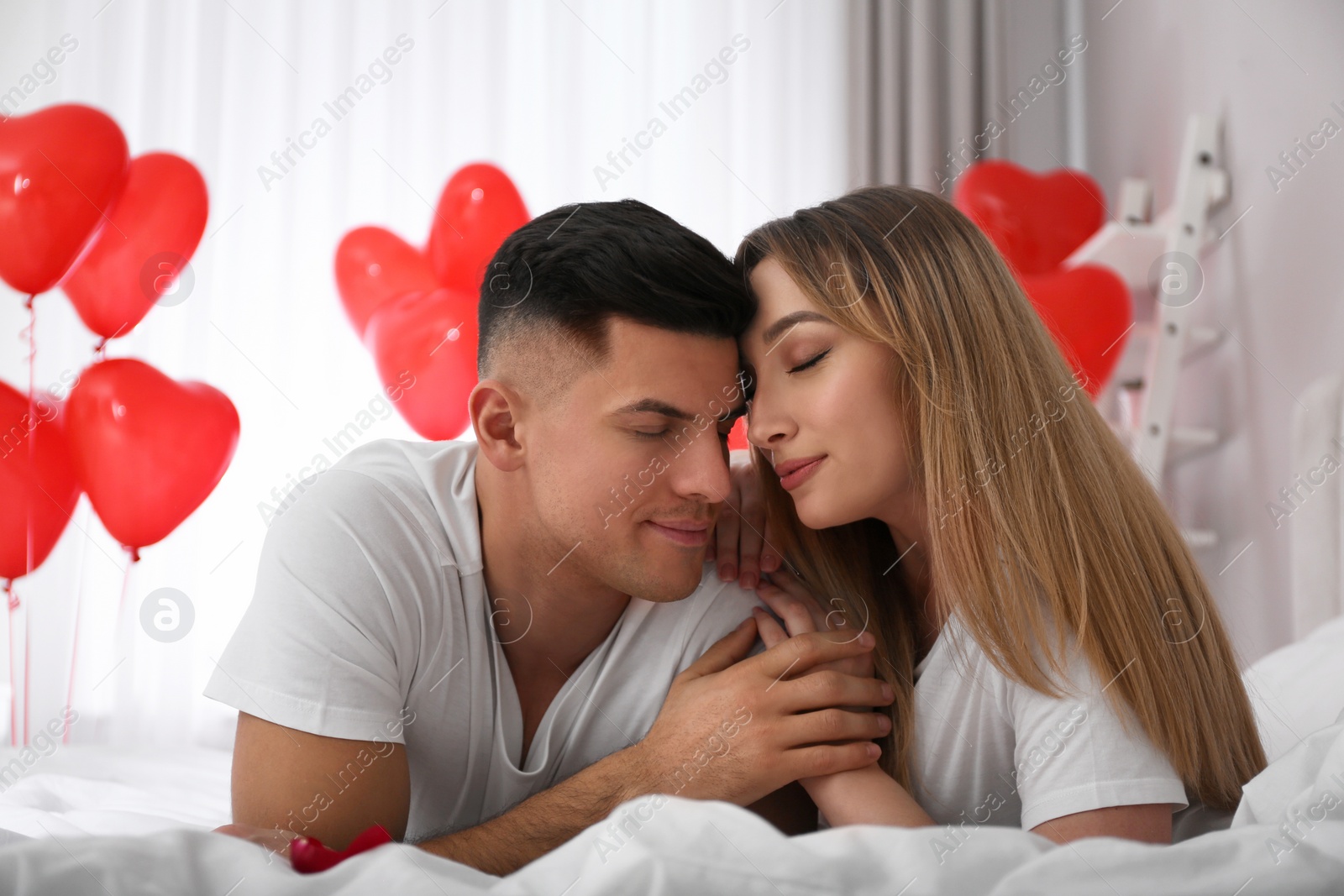 Photo of Lovely couple on bed in room decorated with heart shaped balloons. Valentine's day celebration