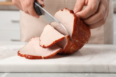 Photo of Man cutting delicious ham at grey marble table indoors, closeup