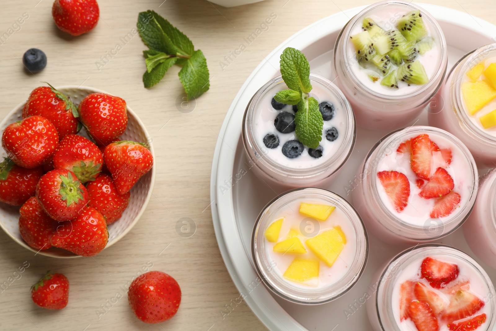 Photo of Yogurt maker with jars and different fruits on wooden table, flat lay