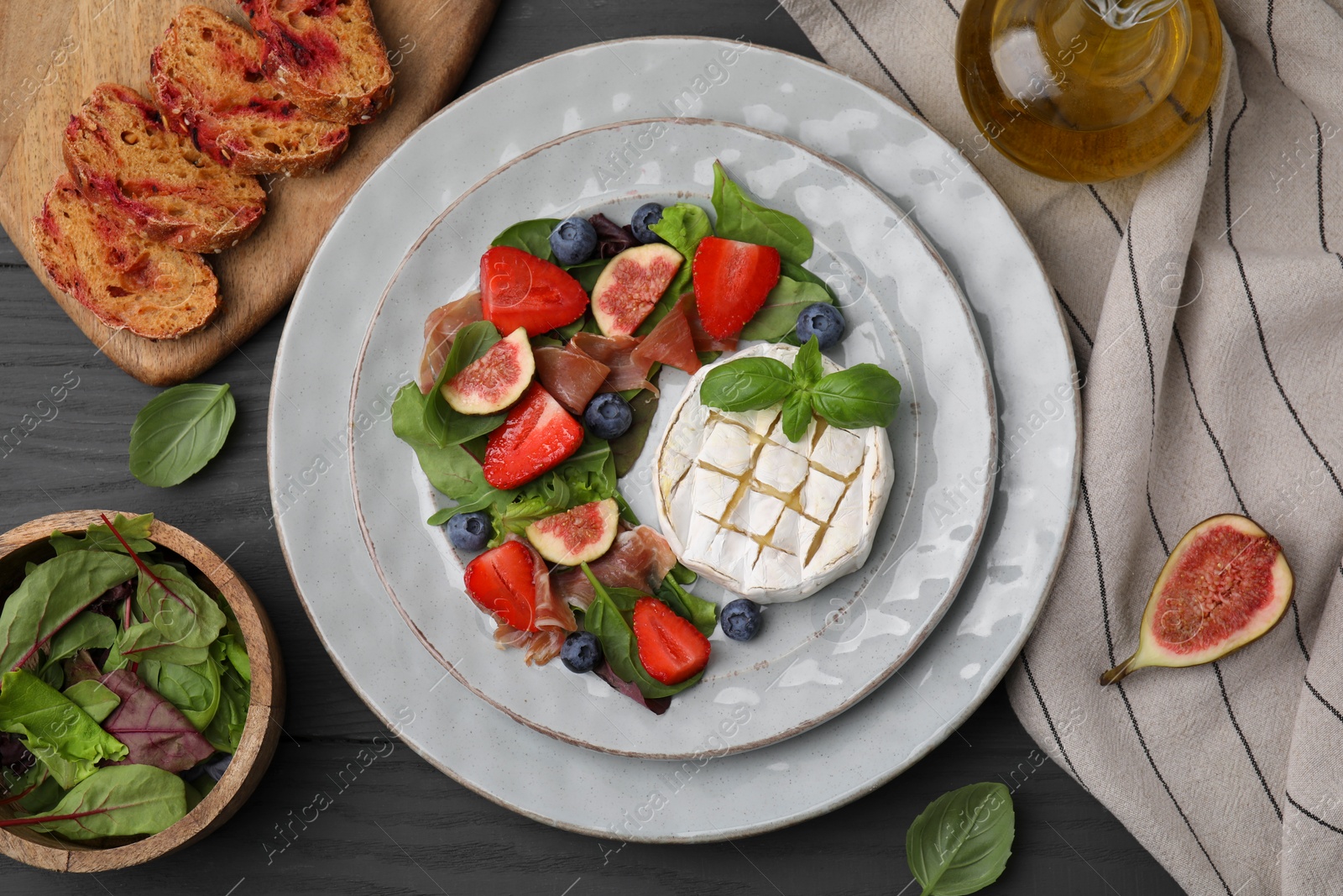 Photo of Delicious salad with brie cheese, prosciutto, figs and strawberries served on grey wooden table, flat lay