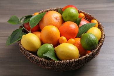 Photo of Different citrus fruits in basket on wooden table