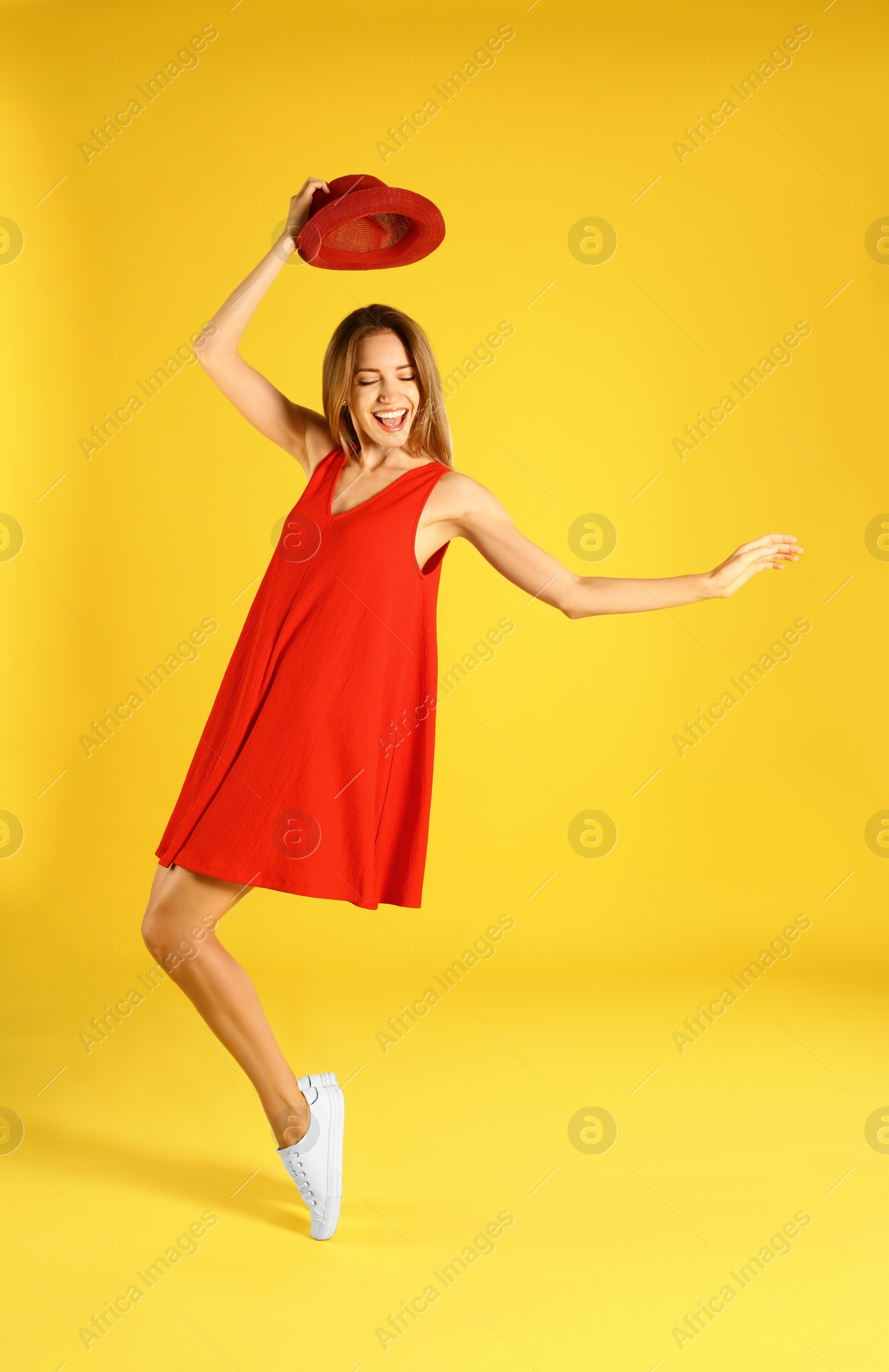 Photo of Beautiful young woman in red dress dancing on yellow background