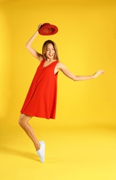 Beautiful young woman in red dress dancing on yellow background