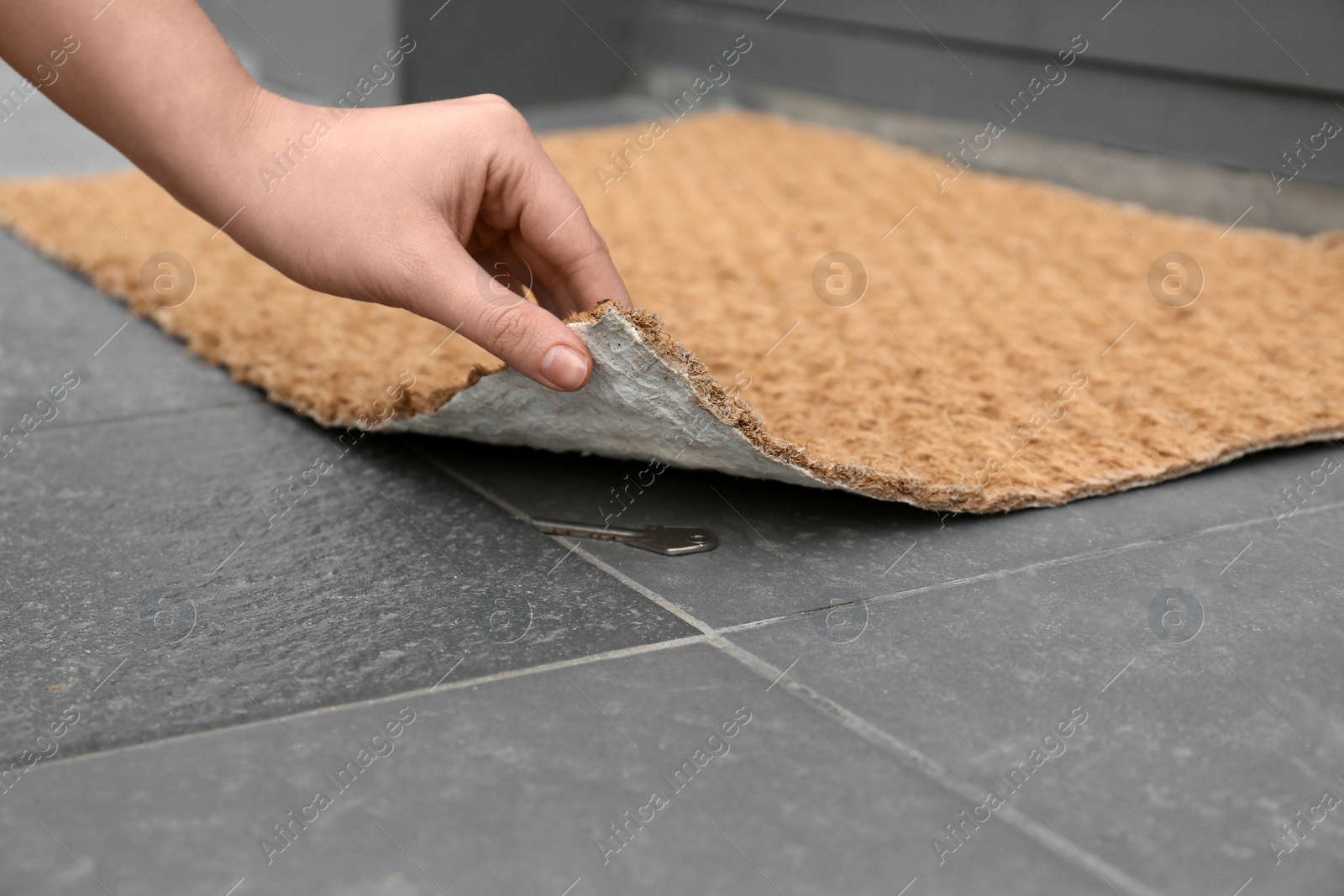 Photo of Woman lifting door mat to reveal key hidden underneath, closeup. Space for text