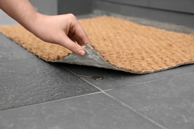 Photo of Woman lifting door mat to reveal key hidden underneath, closeup. Space for text