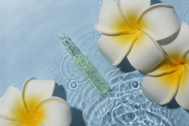 Skincare ampoule and beautiful plumeria flowers in water on light blue background, flat lay