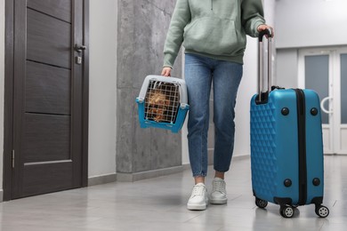 Photo of Travel with pet. Woman with suitcase holding carrier with dog in hall, closeup. Space for text