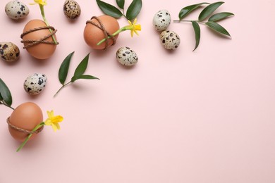 Photo of Festively decorated Easter eggs and green leaves on pale pink background, flat lay. Space for text