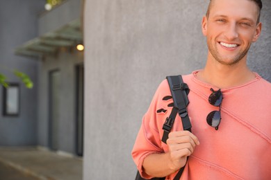 Photo of Handsome young man with stylish sunglasses and backpack near grey wall outdoors, space for text
