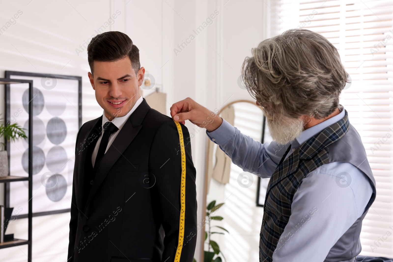 Photo of Professional tailor measuring jacket sleeve length in atelier