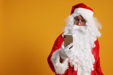 Photo of Merry Christmas. Santa Claus using smartphone on orange background, space for text