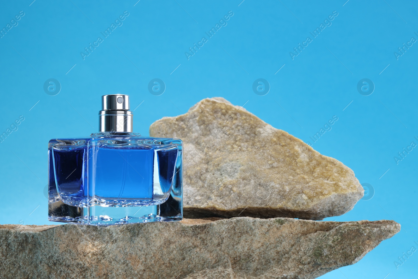 Photo of Stylish presentation of luxury men`s perfume on stones against light blue background