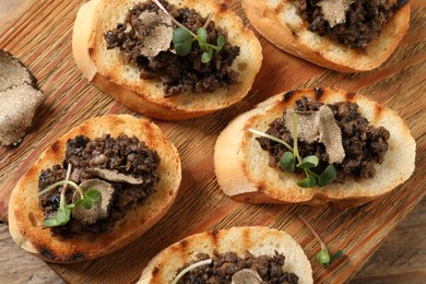 Photo of Delicious bruschettas with truffle sauce and microgreens on wooden table, flat lay