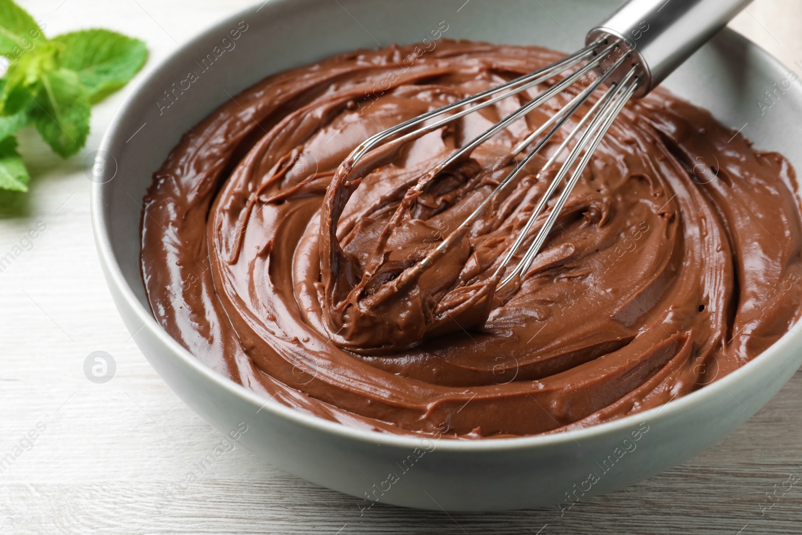 Photo of Whipping chocolate cream with balloon whisk on white wooden table, closeup